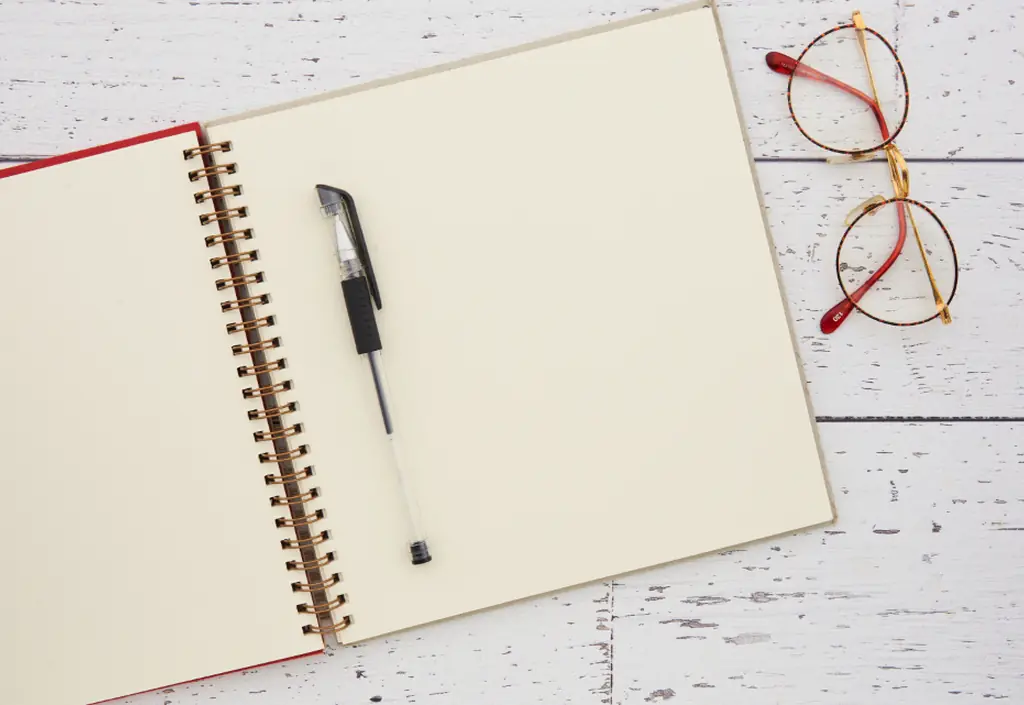 Un carnet ouvert, un stylo et des lunettes sur une table claire