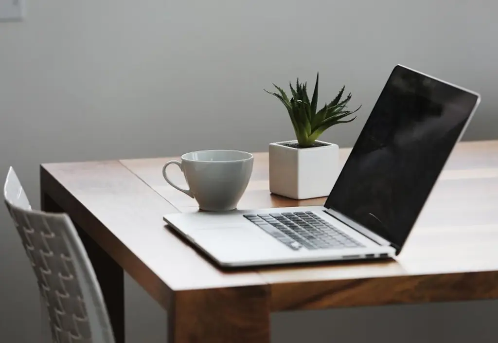 Un ordinateur portable ouvert sur un appel en visio, un bol de petit-déjeuner et un carnet sur une table de cuisine