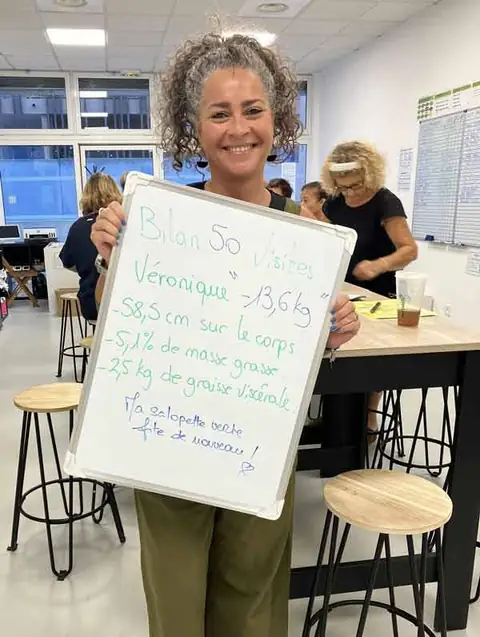 Au club, une membre souriante montre le bilan écrit sur son ardoise