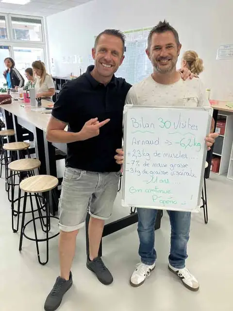 Un coach du club pose avec un membre et l’ardoise de son bilan