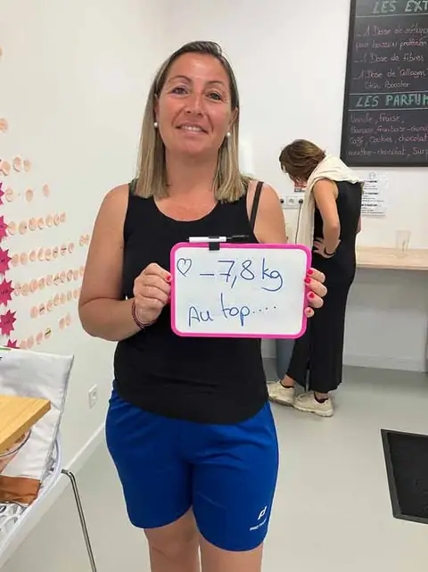 Au club, une membre souriante montre le bilan écrit sur son ardoise